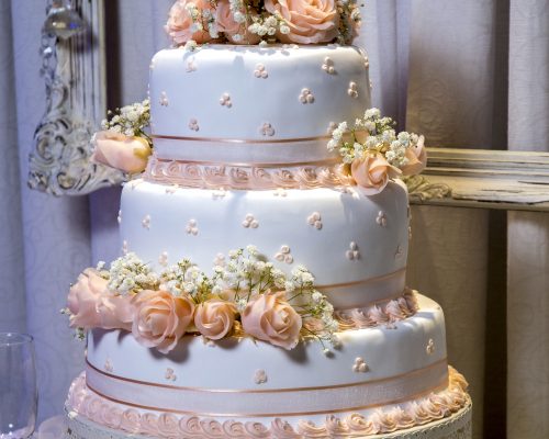 A vertical closeup shot of a beautiful three-layered cake with rose decorations